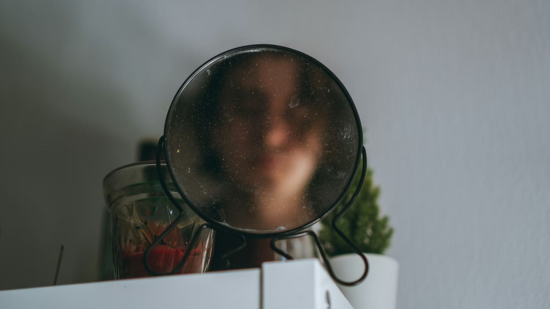 Une personne se regarde dans un miroir rond, on comprend qu'il s'agit du reflet de son visage mais le miroir est recouvert de buée nous empêchant de voir les détails.